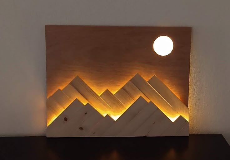 a wooden wall light with mountains in the background and a full moon above it that is lit up