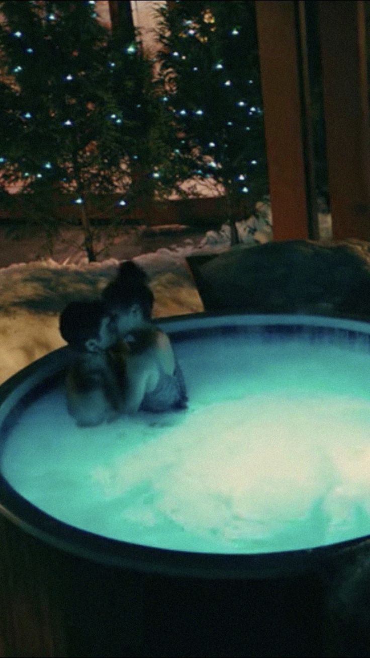 two people are sitting in a hot tub with lights on the outside wall behind them