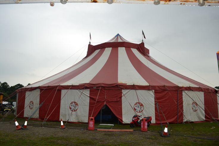 a large red and white circus tent sitting on top of a lush green field