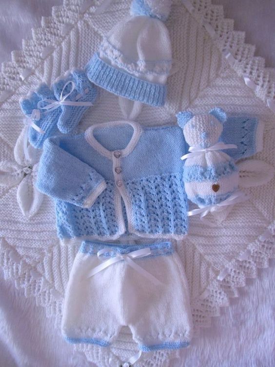 several knitted baby clothes laid out on a doily