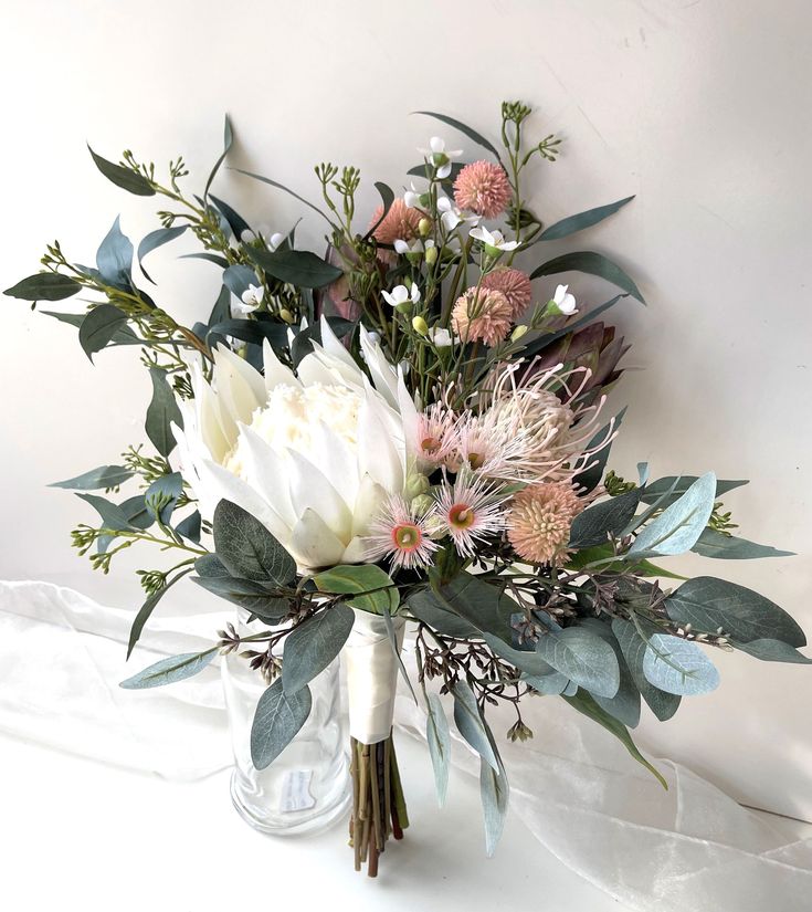 a vase filled with flowers and greenery on top of a white tablecloth covered surface