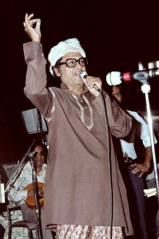 a man wearing glasses and a santa hat sings into a microphone while standing in front of an audience