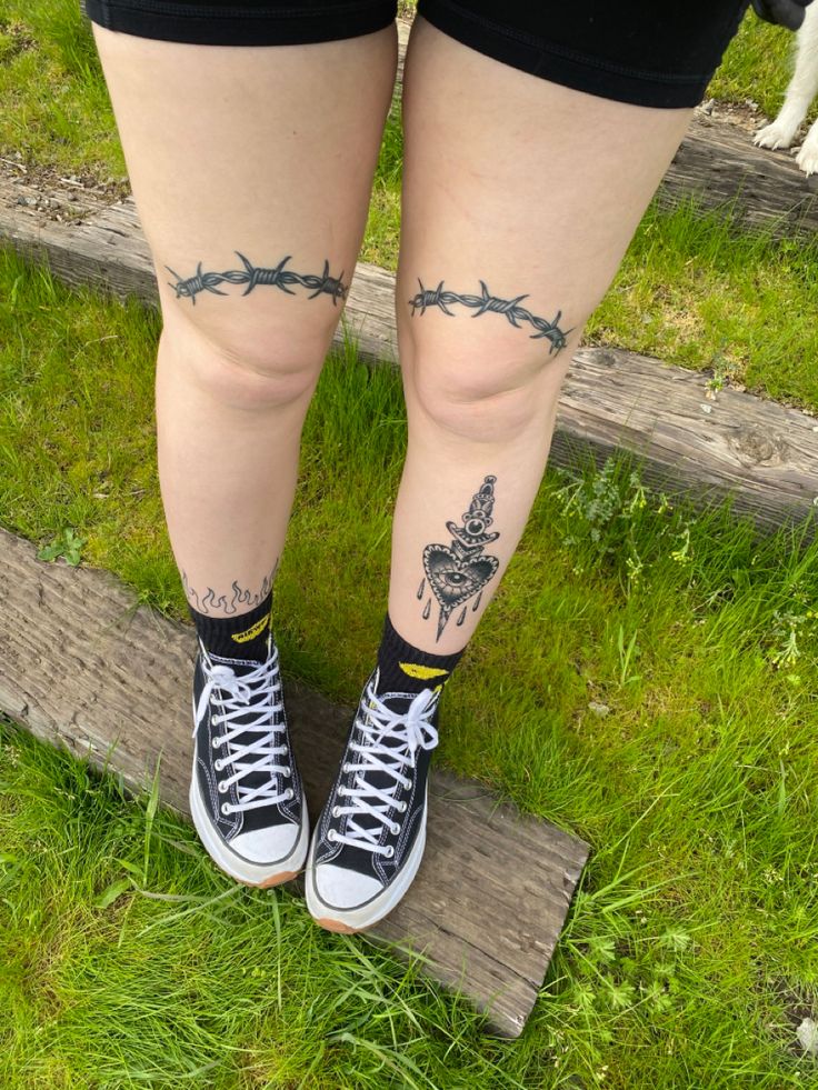 the legs and ankles of a woman with tattoos on them, standing in front of a fence