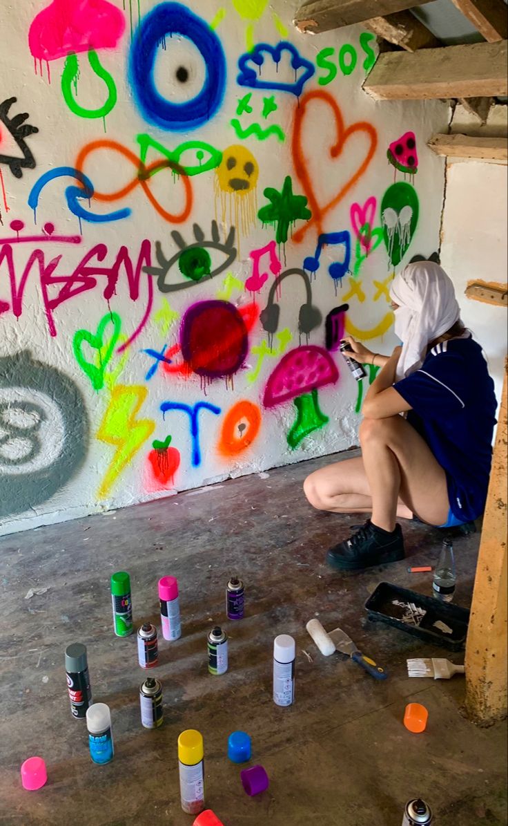 a woman sitting on the floor in front of a wall with lots of colorful graffiti