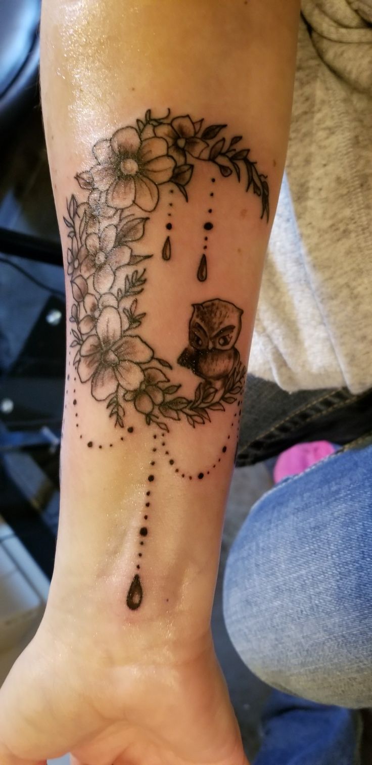 a woman's arm with a tattoo on it that has flowers and an owl