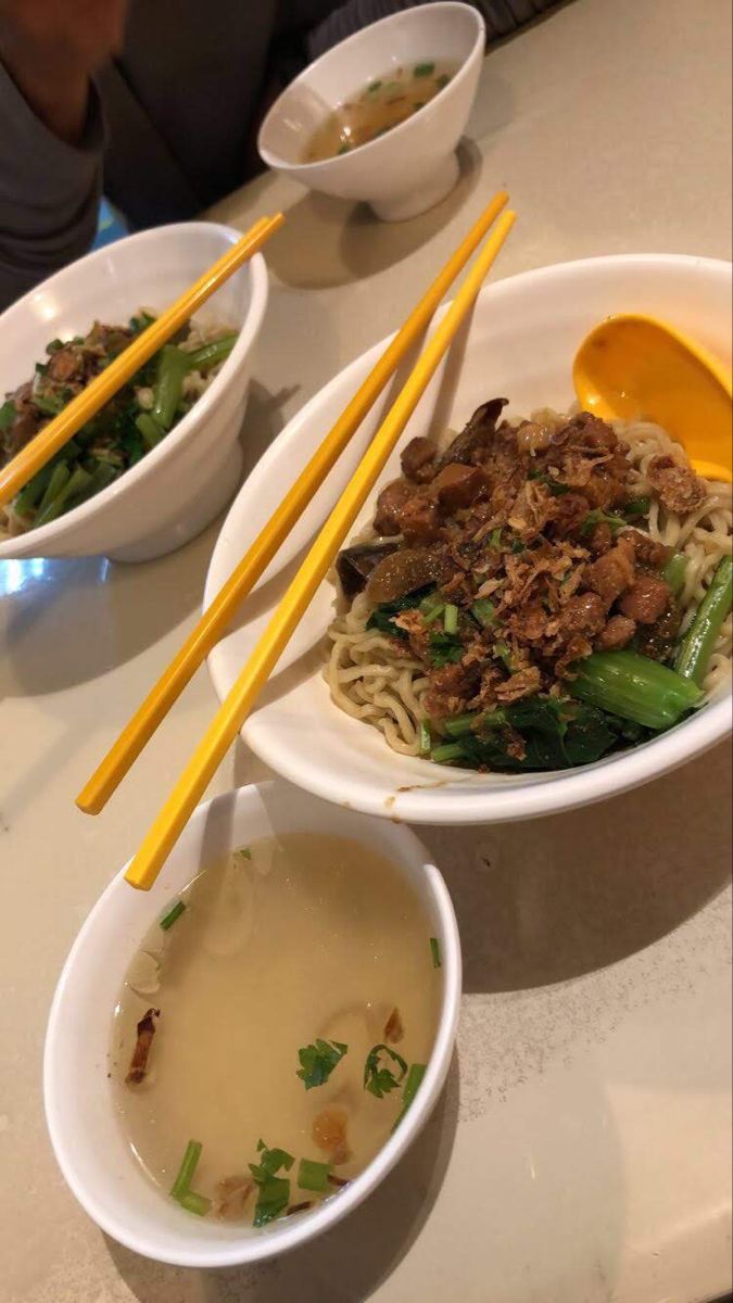 two bowls of food with chopsticks in them on a white table top next to another bowl