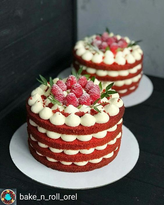 two red velvet cakes with white frosting and raspberries on each cake plate