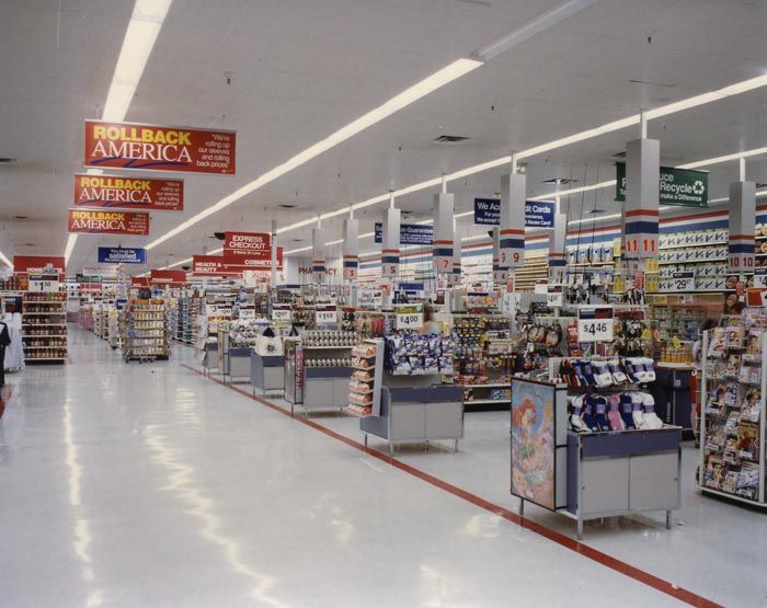 an empty grocery store with signs hanging from the ceiling and people shopping in the aisles