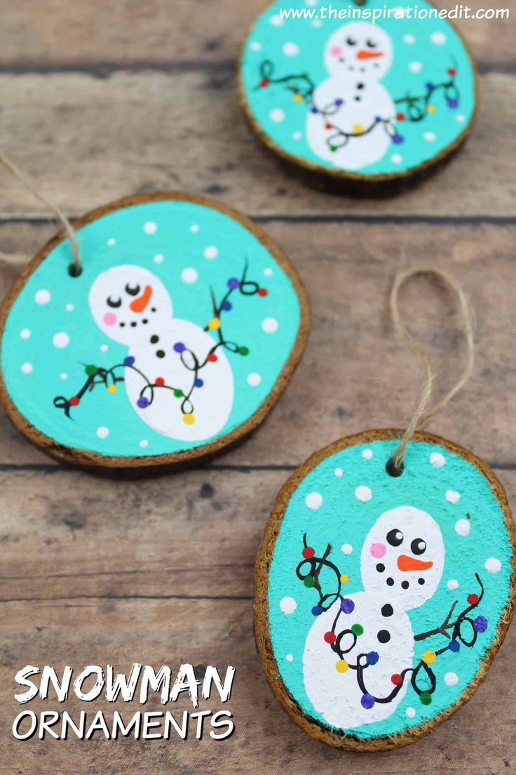 three snowman ornaments are hanging on wood