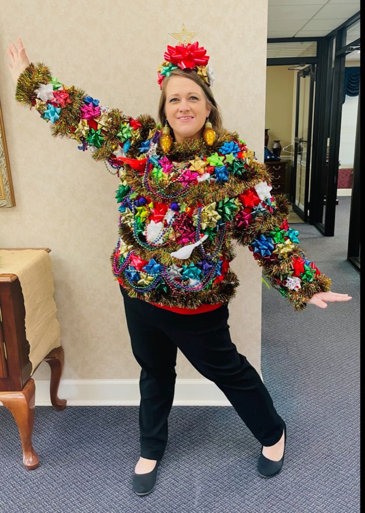 a woman is standing in front of a wall with her arms spread out and wearing a colorful sweater