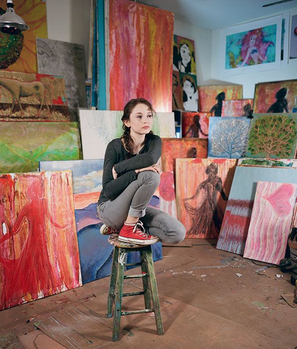 a woman sitting on top of a stool in front of paintings