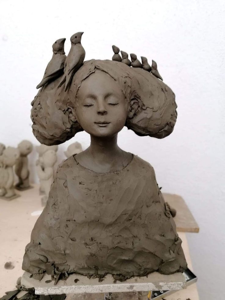 a clay sculpture of a woman's head with birds perched on her hair, sitting on a table