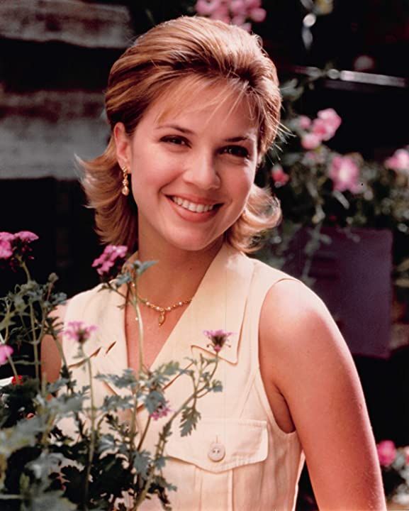 a woman holding a potted plant with pink flowers in it and smiling at the camera