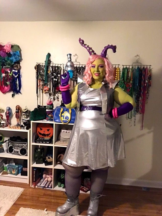 a woman dressed in costume standing next to a wall filled with necklaces and bracelets