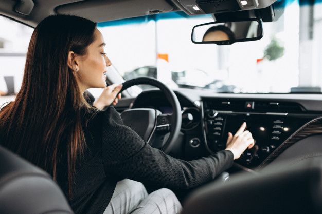 a woman sitting in the driver's seat of a car with her hand on the steering wheel