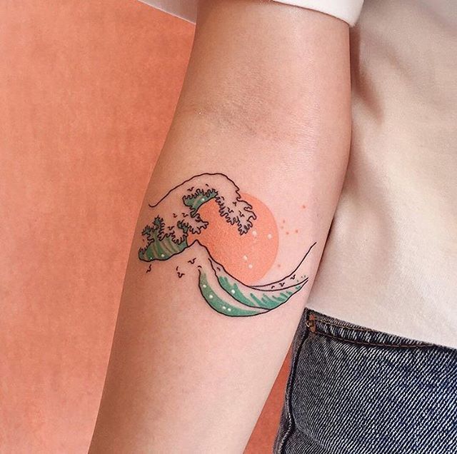 a woman's arm with a tattoo on it that has an image of a wave coming out of the water