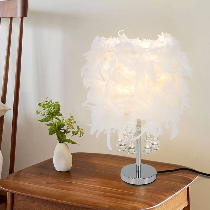 a white lamp sitting on top of a wooden table next to a vase filled with flowers