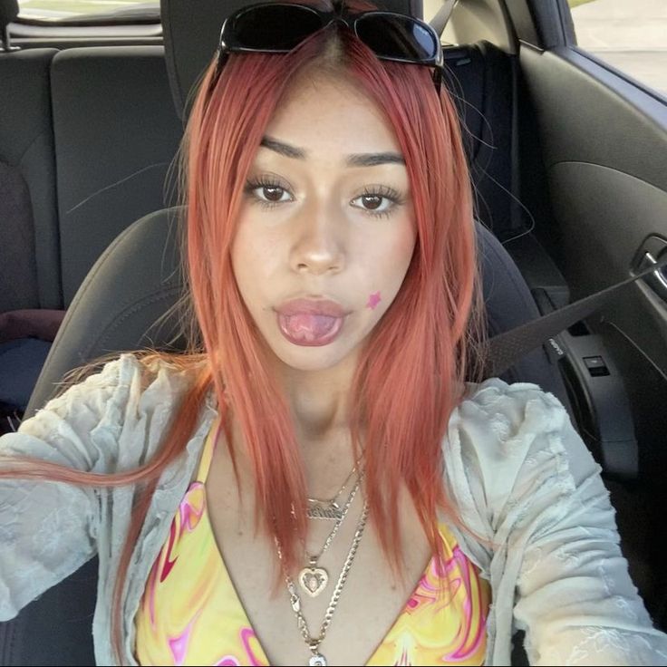 a woman with pink hair sticking out her tongue in the back seat of a car