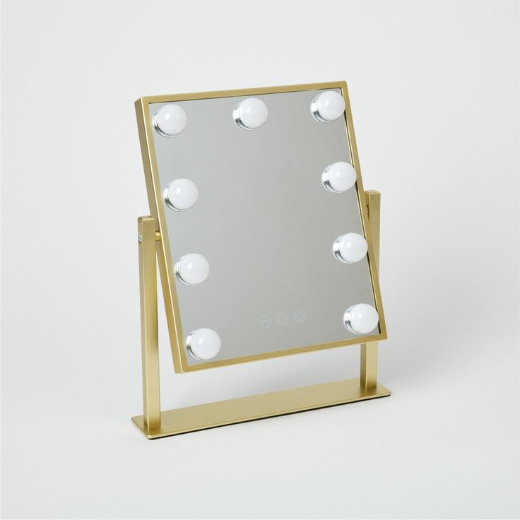 a mirror with lights on it sitting on top of a white table next to a wall