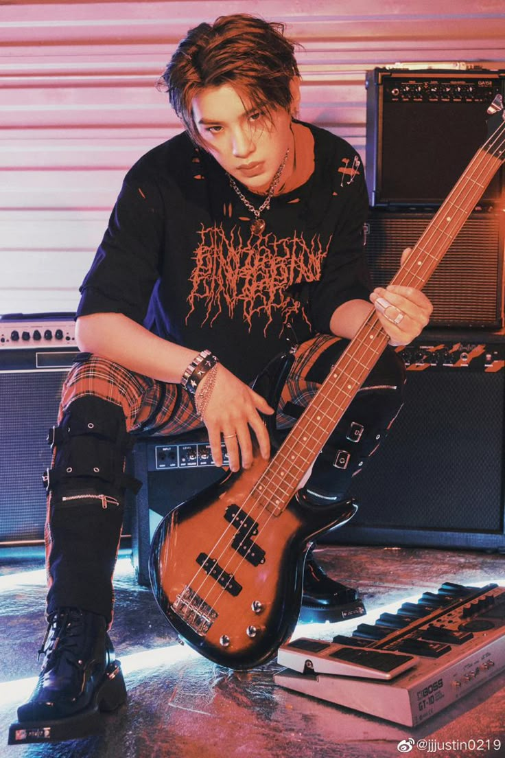 a young man sitting on the floor with his guitar in front of some amps