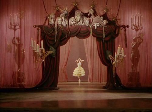 a woman standing in front of a red stage with curtains and chandeliers on it