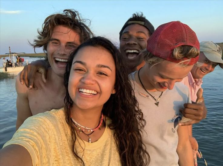 group of young people standing together in front of the ocean with their arms around each other