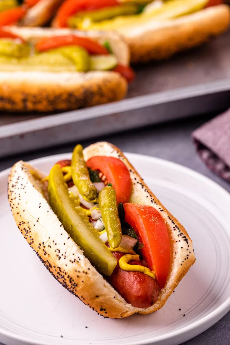 a hot dog on a bun with peppers and onions in the middle, sitting on a white plate