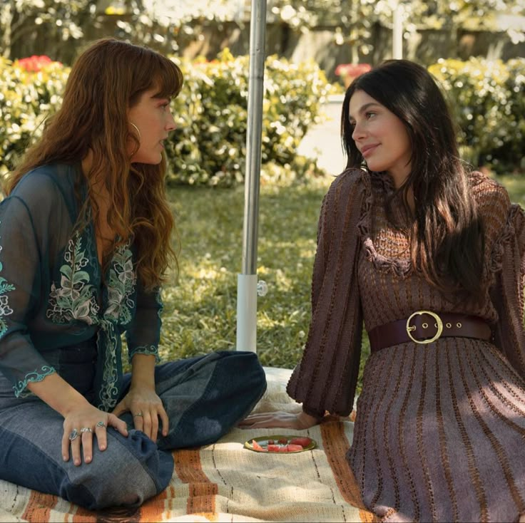 two women sitting on the ground talking to each other in front of an open umbrella