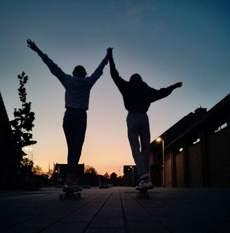 two people standing on skateboards with their arms outstretched in the air at sunset or dawn