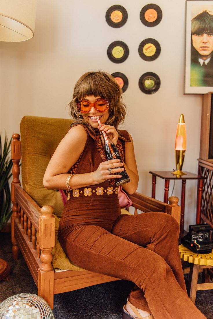 a woman sitting in a chair with her legs crossed and drinking from a straw cup