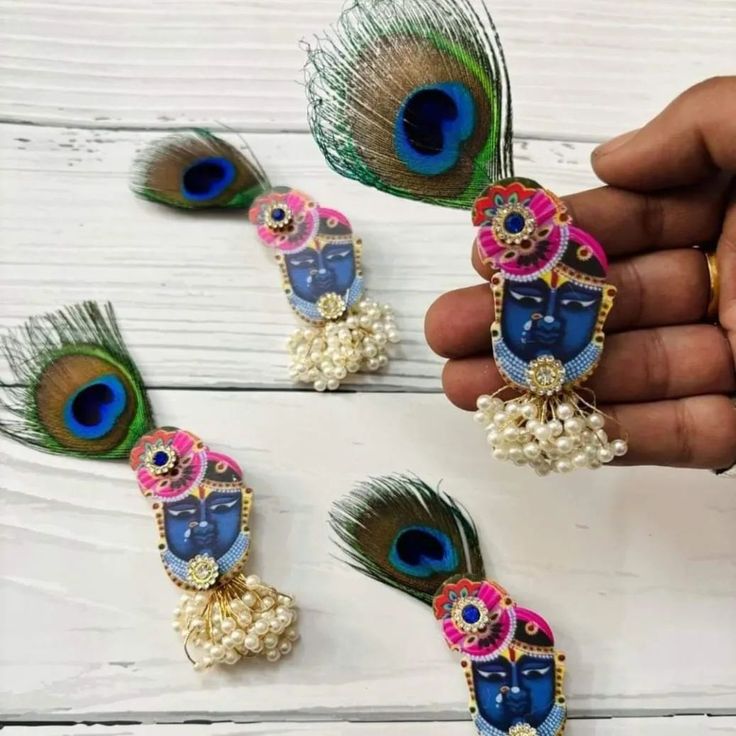 peacock feathers and beads are being held by a person's hand on a white wooden surface