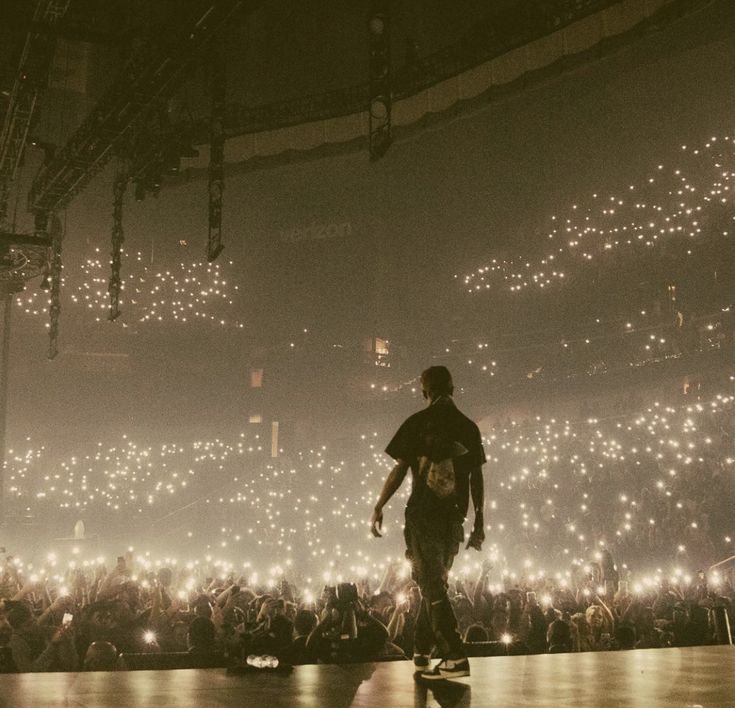 a man on a skateboard in front of a crowd at a concert with lights