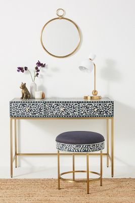 a blue and white desk with a gold frame mirror on the wall next to it