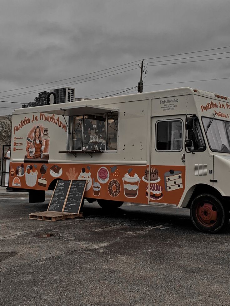 an orange and white food truck parked in a parking lot next to a building on a cloudy day