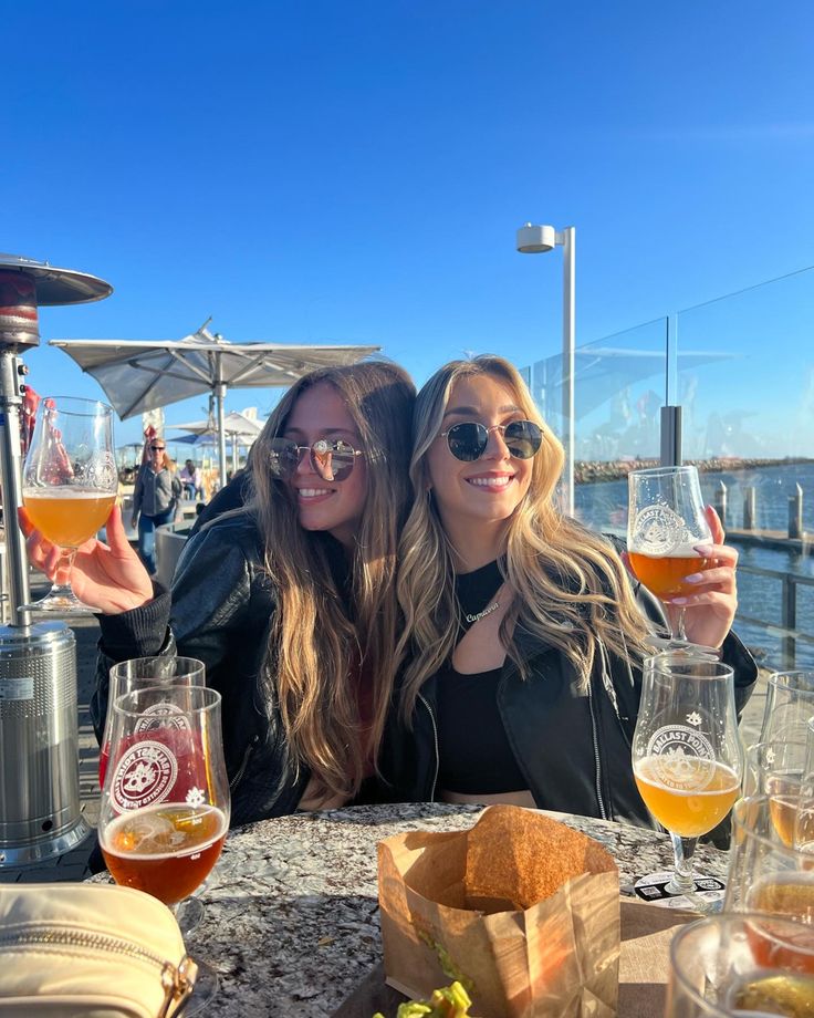 two women sitting at a table with beer and bread in front of them, posing for the camera