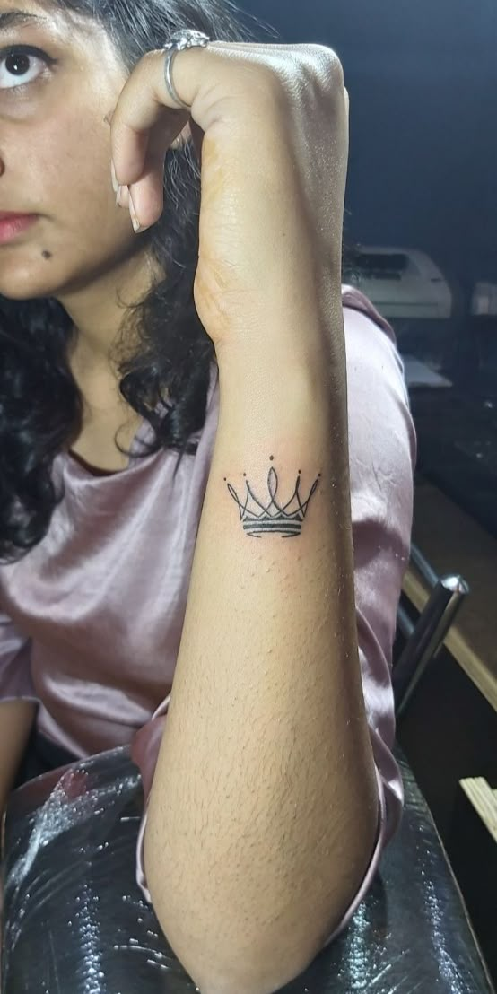 a woman with a small crown tattoo on her left arm, sitting at a table