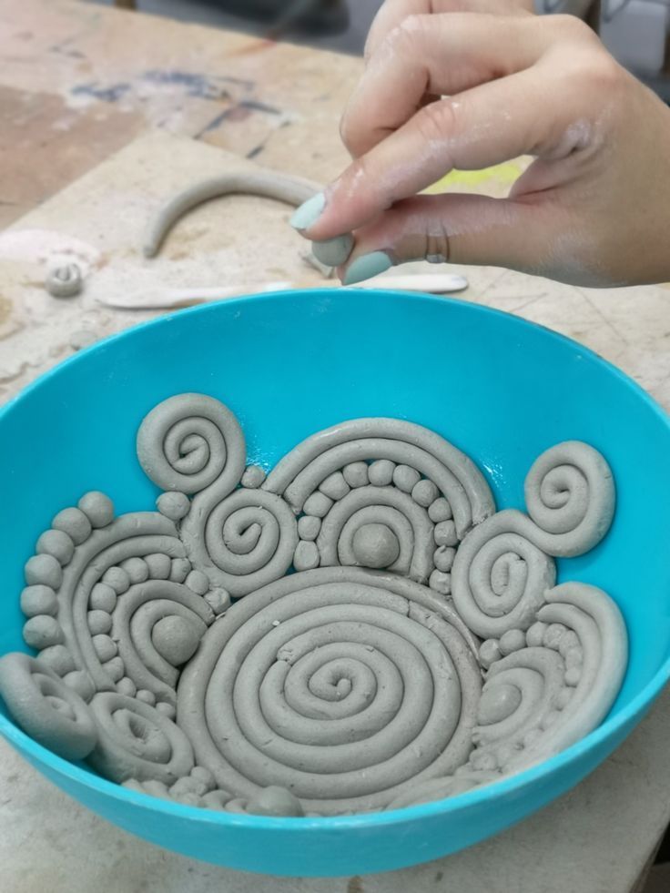 a person is working with clay in a blue bowl on a counter top, while someone's hand reaches for something