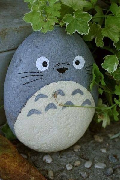 a rock painted like a totoro sitting in front of a potted plant