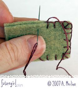 a hand holding a needle and thread on top of a piece of felt