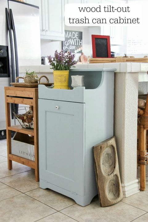 a kitchen counter with a trash can cabinet next to it and a potted plant on top