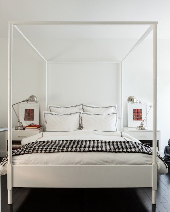 a four poster bed with white sheets and black and white checkered bedspread