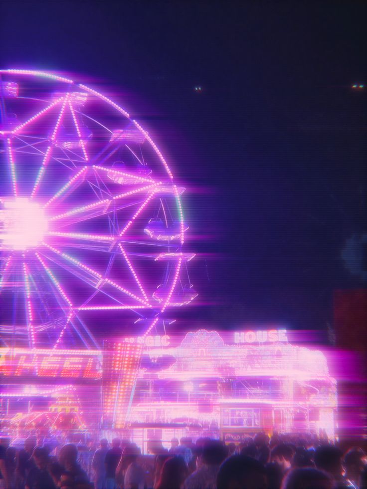 the ferris wheel is lit up at night with people standing around it and in the foreground