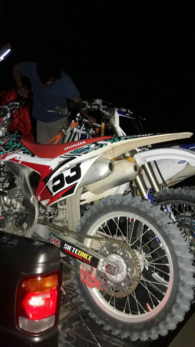 a dirt bike parked on the back of a truck at night with its lights on