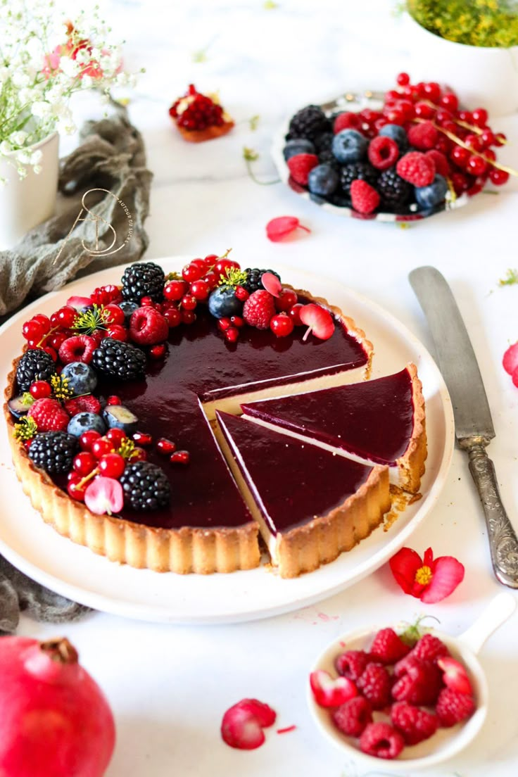 a pie with berries and raspberries on it sitting on a table next to other desserts