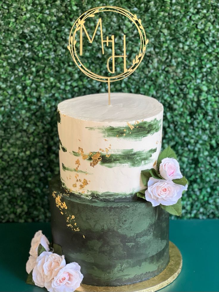 a green and white cake with a gold monogrammed topper sitting on a table