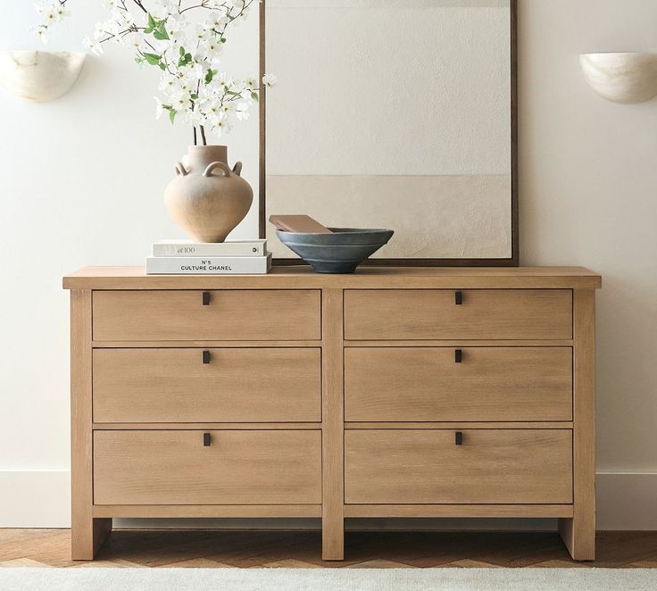 a wooden dresser sitting next to a vase with flowers in it and a mirror on top