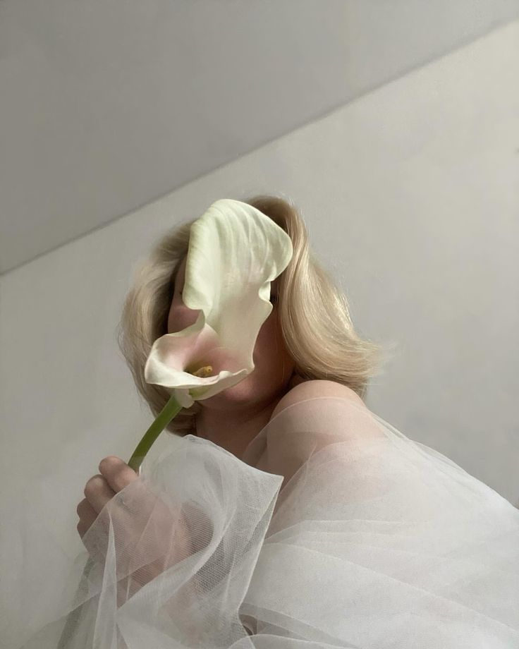 a woman with blonde hair wearing a white dress and holding a flower in her hand