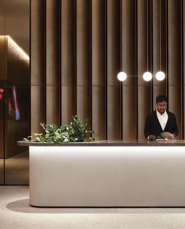 a man sitting at a desk in front of a plant and some lights on the wall