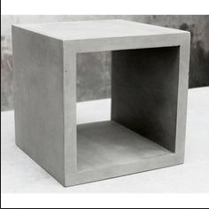 a concrete cube sitting on top of a white table next to a planter and wall