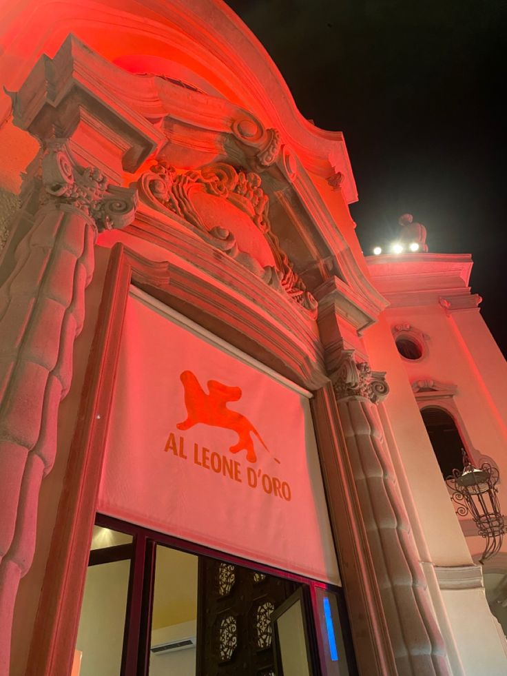 the entrance to an all lion d'oro restaurant lit up with red lights at night